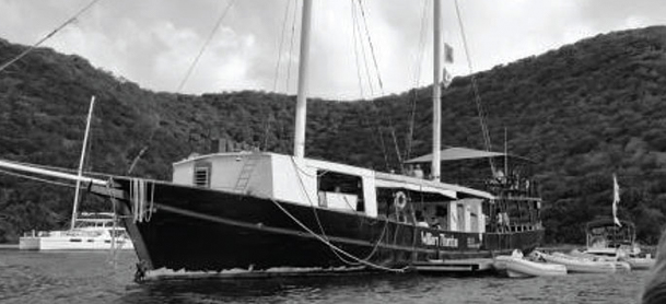 A sailboat rests in the water with hills on the land behind it
